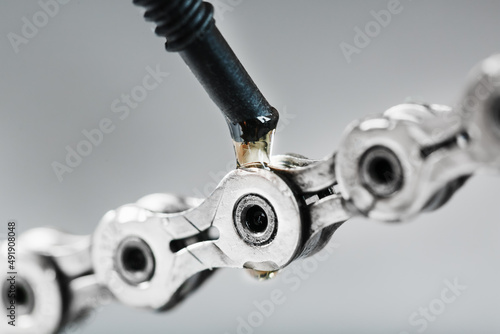 Greasing a bicycle chain with a drop of golden oil close-up on a gray background