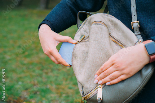 Young woman put smart phone into bag.