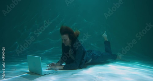 Amazing under water shot of young beautiful workaholic boss business woman using laptop to help clients slow motion. photo