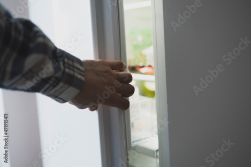 hand opens fridge in the kitchen to take some food