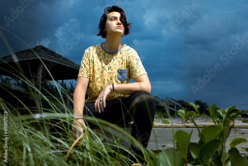 Young male fluid gender female in stormy day with heavy rain clouds in the background posing for camera. Mention the lgbt theme, gender change, sexual freedom and sexuality in youth.