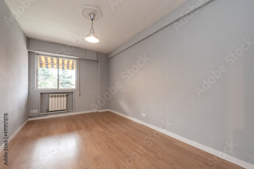 Empty living room with window and white aluminum radiator below  gray painted walls  white rogapie and wooden floorboards