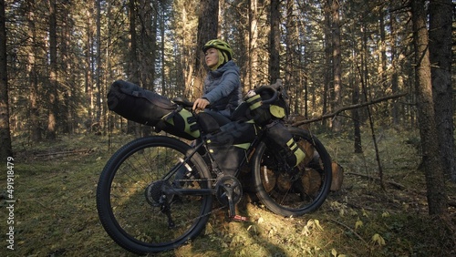 The woman travel on mixed terrain cycle touring with bike bikepacking outdoor. The traveler journey with bicycle bags. Stylish bikepacking  bike  sportswear in green black colors. Magic forest park.