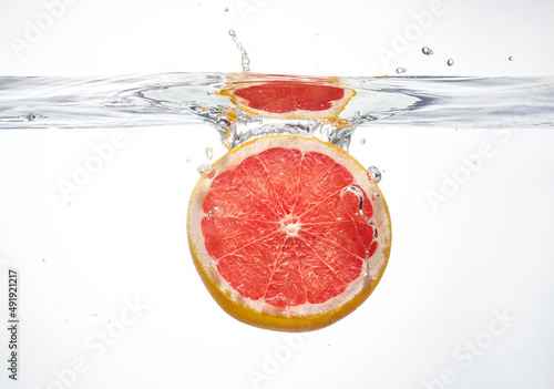 A single piece of fresh red grapefruit being splashed into water. Beautiful juicy piece of citrus grapefruit taking a plunge into water. Fresh natural orange citrus flavour.