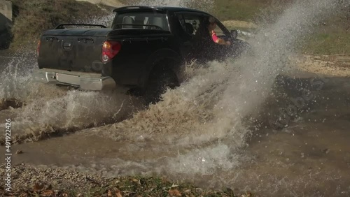 a pickup truck drives at speed through a small pond