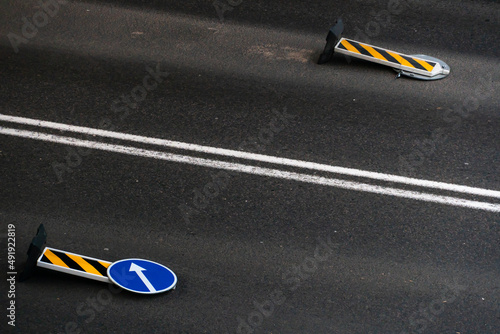 A road sign with a white arrow on a blue background lies on the roadway. A strong wind knocked over a road sign. Double marking line on the asphalt of the road