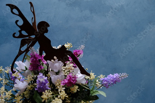 a little fairy perched on top of a bouquet of colorful flowers and blue background
