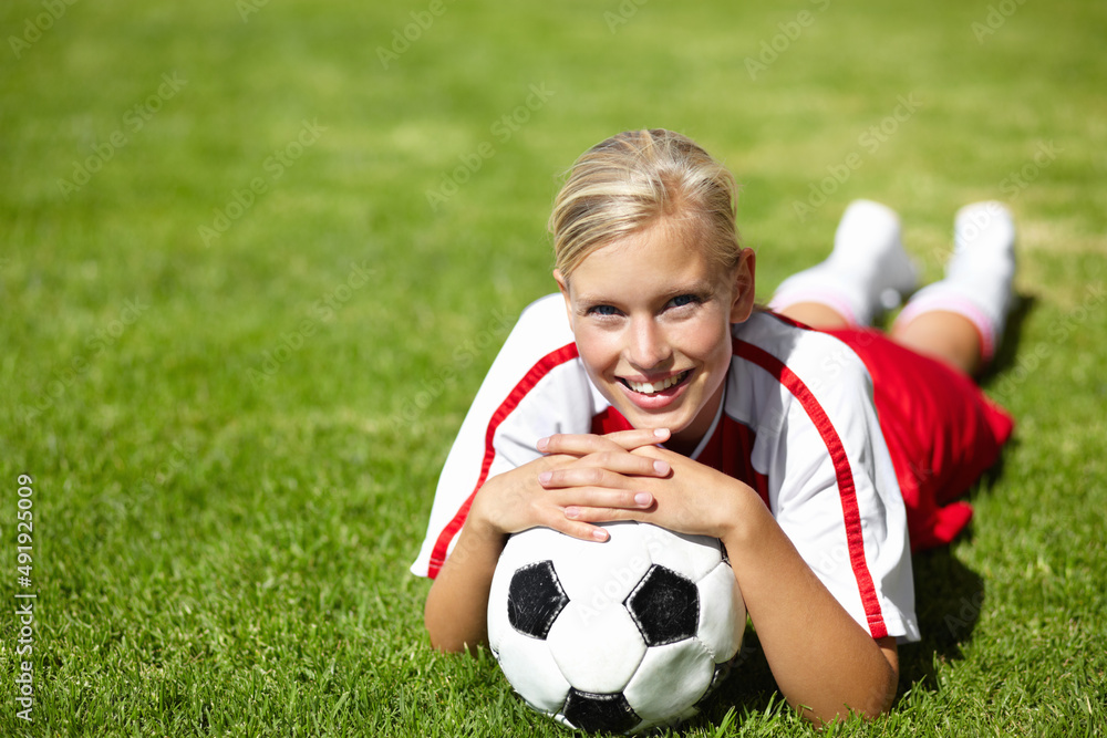 © C Mcdonald/peopleimages.com - Shes the team captain. Portrait of an attractive female football player lying chest down on the grass and leaning on a soccer ball.