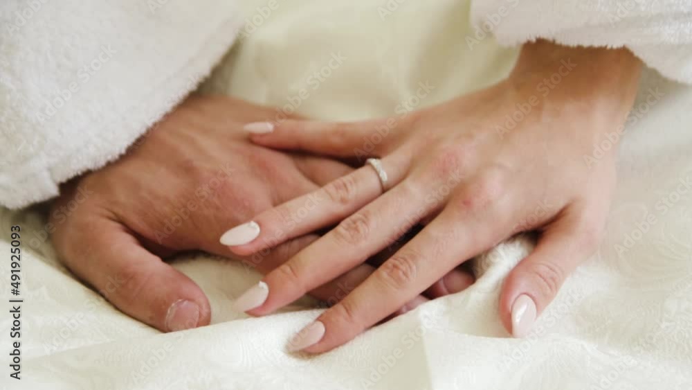 Man and woman in love touch with their hands on white bed. Husband and wife with wedding rings on their fingers close-up Man and woman in love touch with their hands on white bed. Husband and wife with wedding rings on their fingers close-up