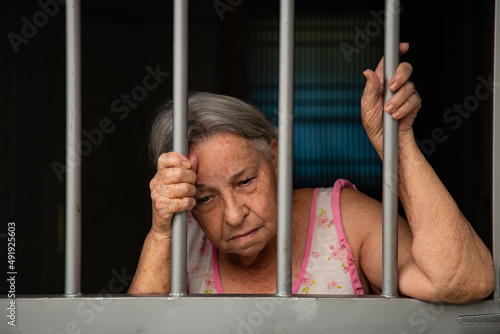 Mulher idosa com cara triste atrás das grades no portão. photo