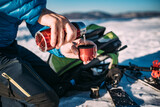 Mężczyzna nalewa gorącą herbatę lu kawę z termosu w słoneczny dzień na wyprawie skitouringowej
