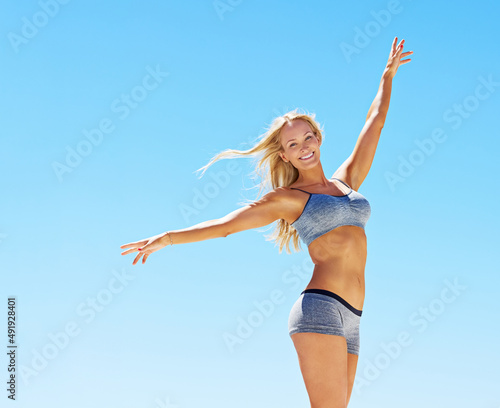As perfect as the weather. Portrait of a young woman in workout gear standing against a blue sky.