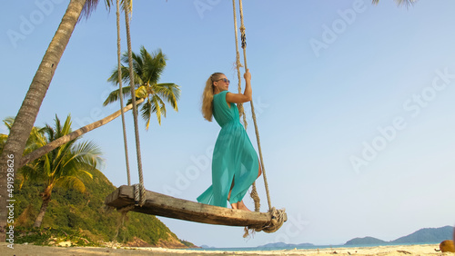 Pretty woman swinging on a swing on a tropical beach, on shores of the turquoise sea. Concept travel, walks, rest in sea, tropical resort coastline relaxation traveling tourism summer holidays