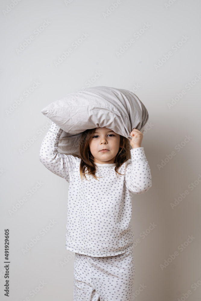 Portrait of pretty caucasian girl in white pyjama and pillow in studio white background 