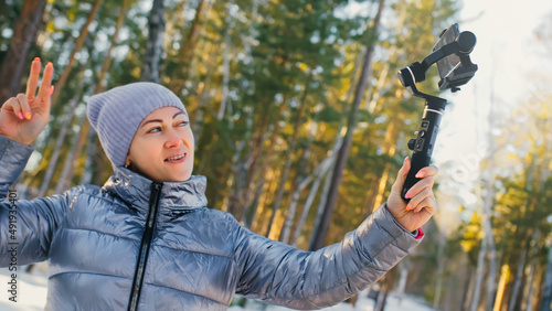 The Woman Professional Videographer Holding Smartphone on 3-axis Gimbal Stabilization Device in Winter. Pro Equipment Helps to Make High Quality Video on Phone. Cinematographer Operator. Slow Motion