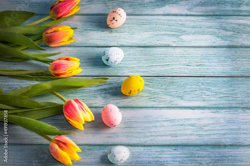 spring tulips and Easter eggs in pastel colors on a blue wooden background.