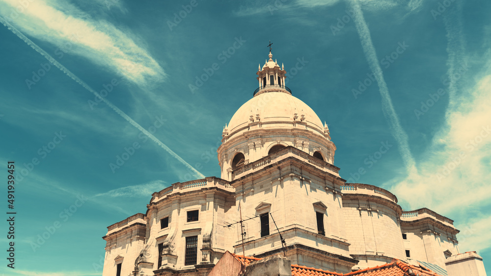 A wide-angle view from the bottom of The Church of Santa Engracia or another name National Pantheon on a very sunny day, with blue sky with clouds and aircraft contrails behind the building