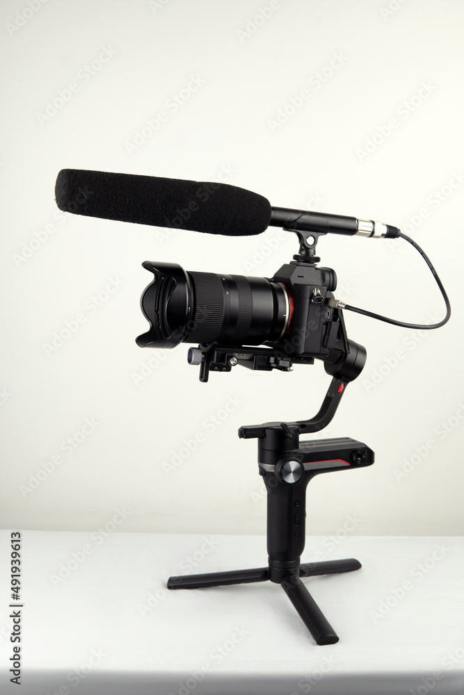 mirrorless camera and a connected microphone mounted on an electronic stabilizer on a white background
