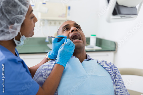 Portrait of latin american man sitting with open mouth during dental checkup at dentist
