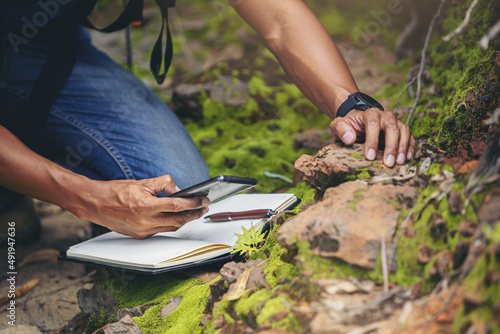 Biologist or botanist recording information about small tropical plants in forest. The concept of hiking to study and research botanical gardens by searching for information.