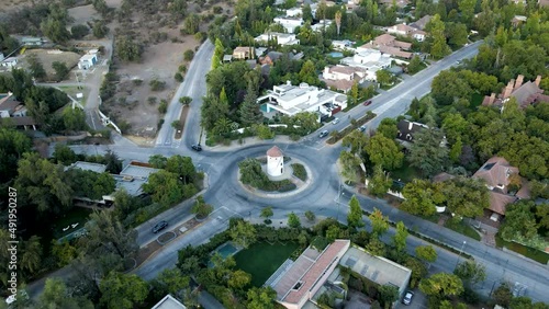 Aerial dolly in lowering on Leonidas Montes windmill tower in roundabout with cars driving surrounded by trees, Lo Barnechea, Santiago, Chile photo