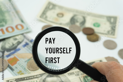 Magnifying glass showing the words "Pay yourself first".Background of banknotes and coins.basic concepts of personal finance.