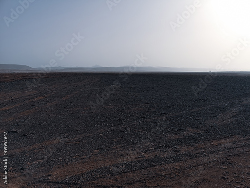 Dark rocky African terrain, Boa Vista Island, Cape Verde. Clear blue sky, brown landscape, distance hills. Selective focus on the details, blurred background.