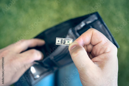 Obraz na plátne A male businessman opens a black wallet and pulls out a hundred-dollar bill on a green background