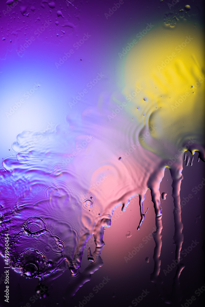 drops and splashes of water spreading on glass on a bright colored background