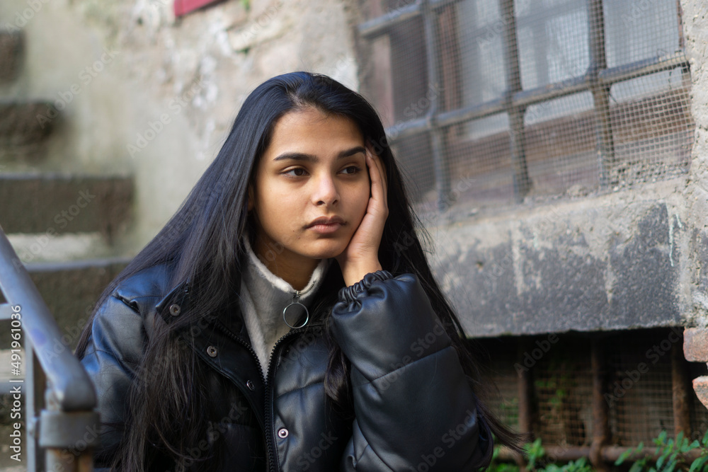 Sad, tired looking young woman sitting outdoors and holding her head with her hand. Indian ethnicity. Sad, tired looking young woman sitting outdoors and holding her head with her hand. Indian ethnicity.