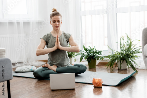 Athletic woman doing yoga and watching online lessons on laptop, exercising in living room
