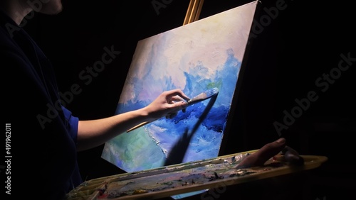 Artist copyist paint seascape with ship in ocean. Craftsman decorator draw as boat sail on blue sea with acrylic oil color. Draw finger, brush, knife palette. Indoor. Dark magic cinematic look.
