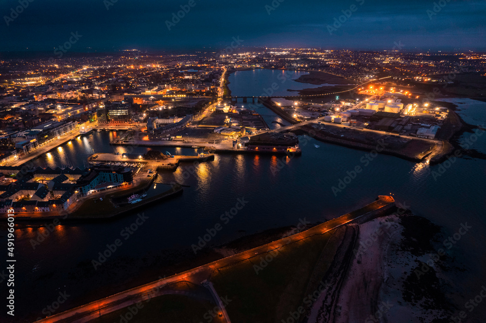 Galway city illuminated at night, port area. Aerial high point view. Dark scene. Town at night. Popular travel destination. Business and educational center. City lights glow in the dark.