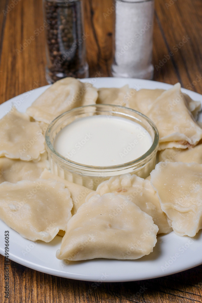 Serving of polish dumplings with small bowl of sour cream, close up. Traditional simple food. Serving of polish dumplings with small bowl of sour cream, close up. Traditional simple food.