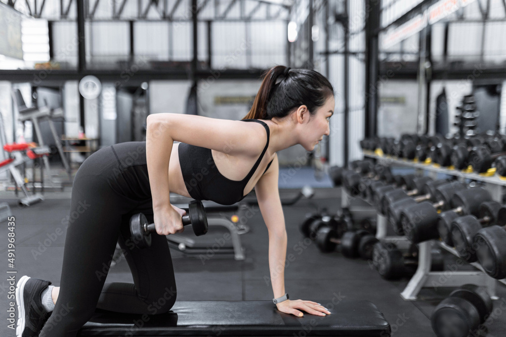 exercise concept The female exercise beginner doing dumbbell workout by resting her left knee and left hand on the bench and raise her right elbow up with a dumbbell in her hand exercise concept The female exercise beginner doing dumbbell workout by resting her left knee and left hand on the bench and raise her right elbow up with a dumbbell in her hand