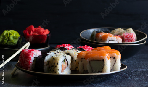 Sushi rolls with wasabi, ginger, bamboo chopsticks on dark background. Side view