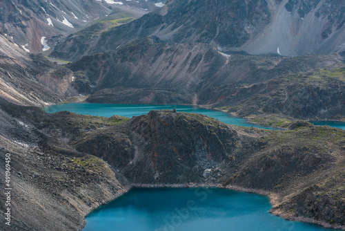 Beautiful group of azure and turquoise mountain lakes at various heights among black rocks in bright sun. Two blue alpine lakes at different highs among sunlit black green rocky hills in highlands.