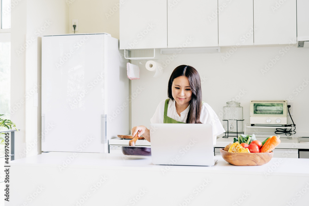 パソコンを見ながら料理する女性(笑顔)
パソコンを見ながら料理する女性(笑顔)