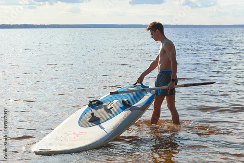 Nizhny Novgorod,Russia-08.08.2020: Young fit active person with stand up paddle board and oar goes in water to exercise. Sup surfing in summer