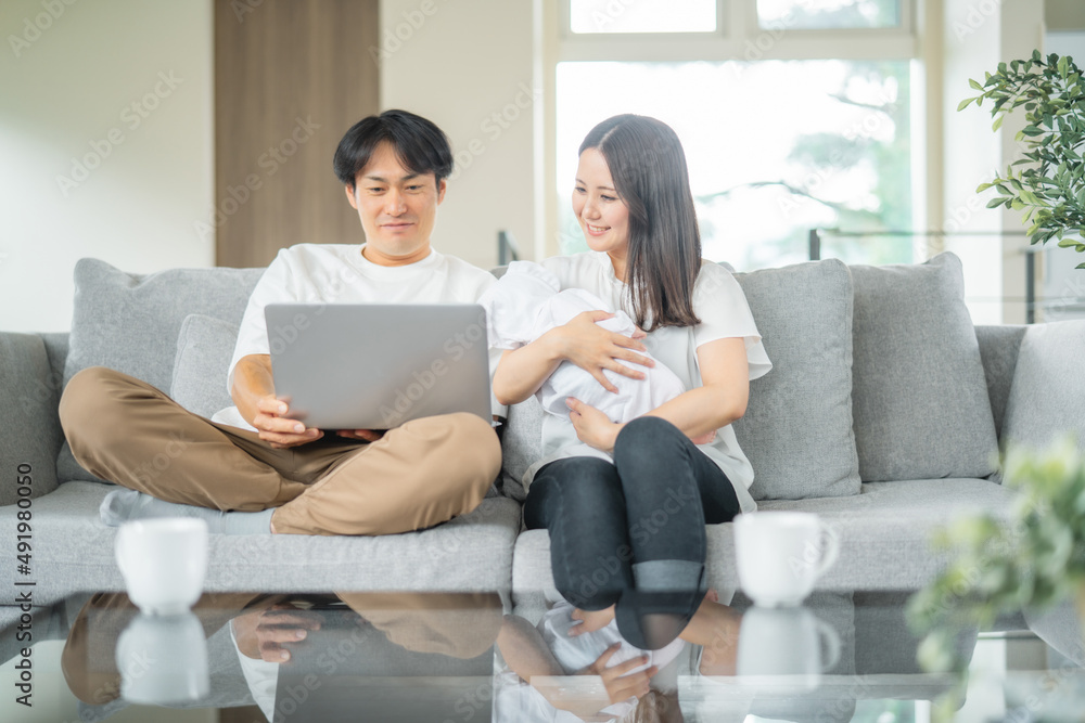 部屋でパソコンを使う赤ちゃんを抱く男女
