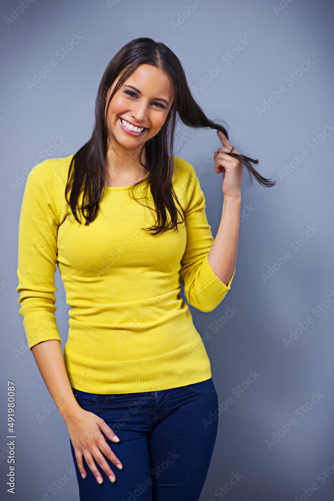 Feeling flirty. Studio portrait of a beautiful young woman twirling her hair against a blue background. Feeling flirty. Studio portrait of a beautiful young woman twirling her hair against a blue background.