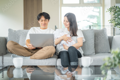 部屋でパソコンを使う赤ちゃんを抱く男女
