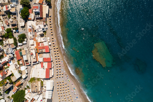 Ujęcie z drona na piękną plażę w Matala, na wyspie Kreta w Grecji, turkusowa woda i pomarańczowy piasek, rzędy parasoli plażowych