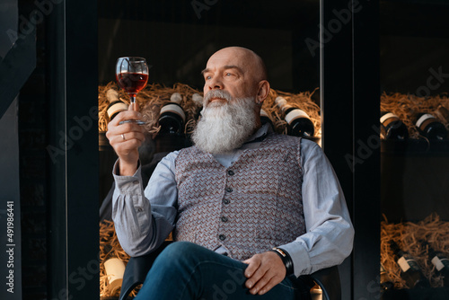 satisfied elderly winemaker looking at the glass of wine in his hand.