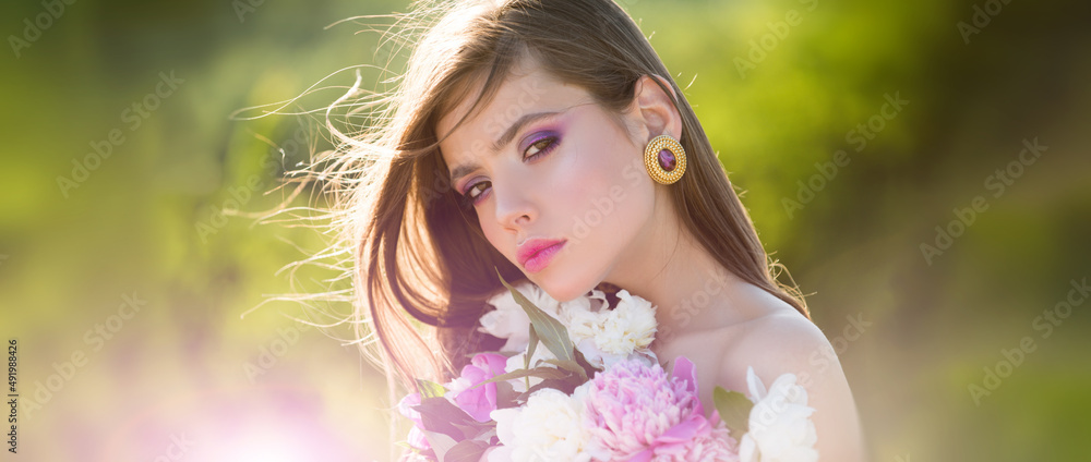 Fototapeta premium Natural beauty face. Young beautiful sexy carefree woman posing on the spring background. Summer model holding flowers in hands outdoors.