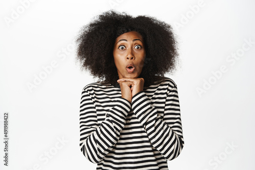 Image of excited african american woman looking with amazement, staring astonished, fascinated, watching smth breathtaking, standing over white background