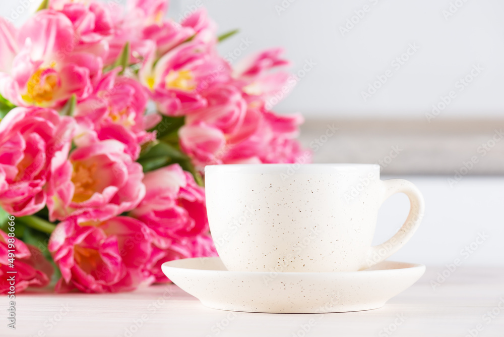 A cup of coffee with a bouquet of pink tulips on the table.