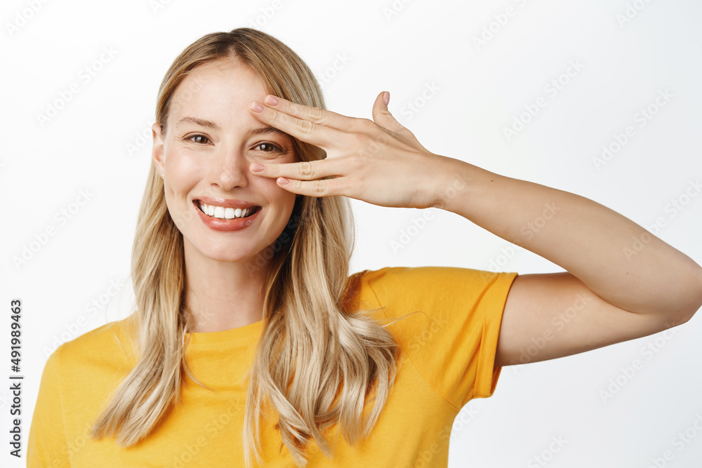 Portrait of happy blond woman laughing, smiling and looking authentic, touching clear glowing skin, perfect face without makeup or blemishes, standing over white background Portrait of happy blond woman laughing, smiling and looking authentic, touching clear glowing skin, perfect face without makeup or blemishes, standing over white background
