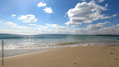 Time-lapse of a seascape on a clear sunny day, clouds descend low over the water in dynamic motion, sunlight reflects on the water, waves arrive on the sandy shore and go back to the sea