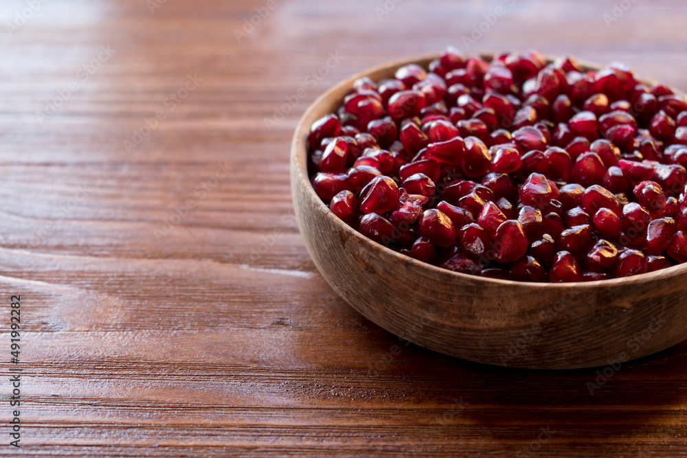 red pomegranate seeds in a wooden bowl on an old wooden background red pomegranate seeds in a wooden bowl on an old wooden background